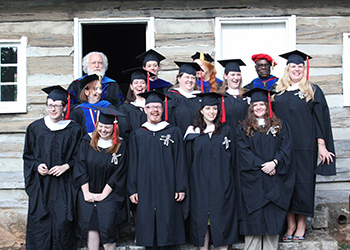 Graduates of the program standing in front of a log cabin