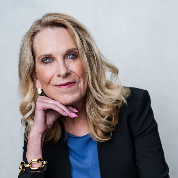 Woman with medium length blonde hair wearing a black blazer and blue shirt