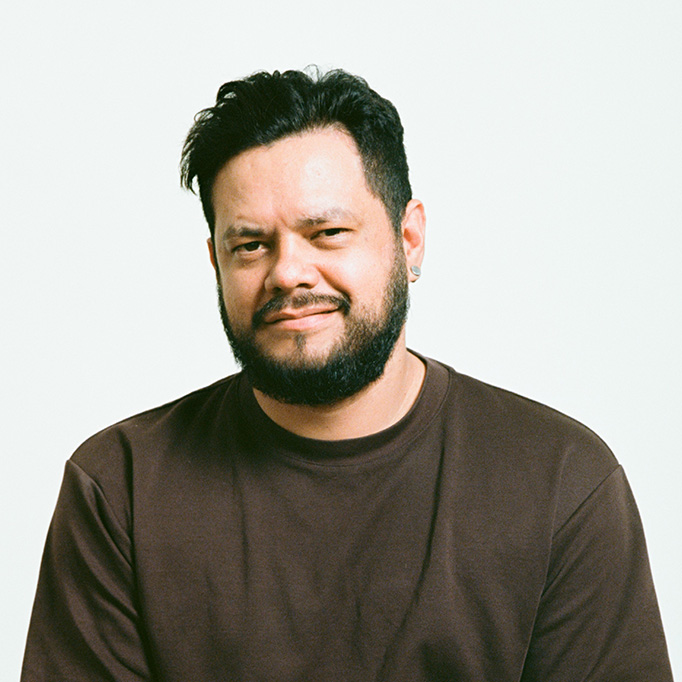 Man with black hair and a beard in a brown t-shirt