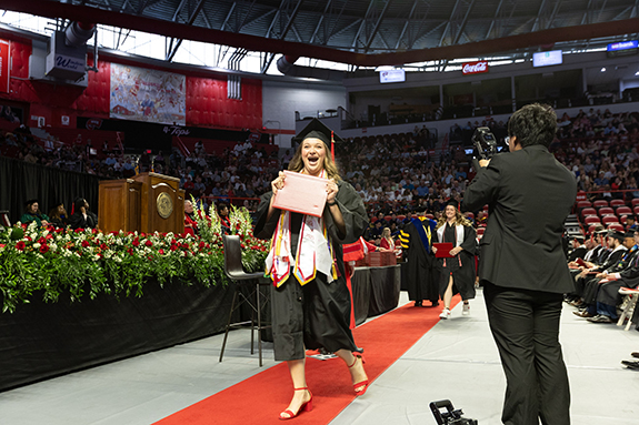 WKU graduate walking on the red carpet while holding diploma and having photo taken