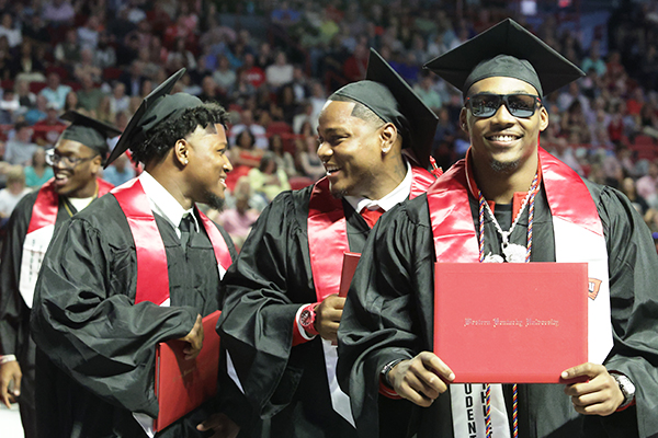 WKU graduates posing for a photo with diploma covers