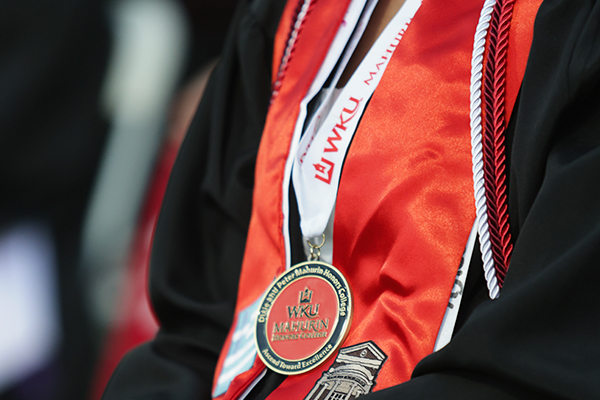 Medals, stoles, and cords draped over the gown of a WKU graduate