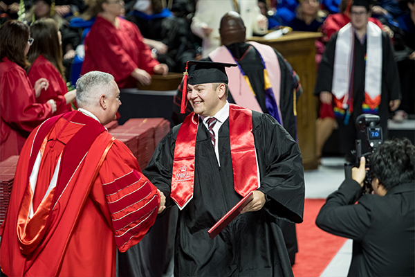 WKU graduate walking on the red carpet while holding diploma and having photo taken