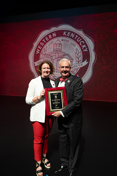 2026 Spirit of WKU award winner Dr. Corinne Murphy holds a plaque next to President Timothy C Caboni