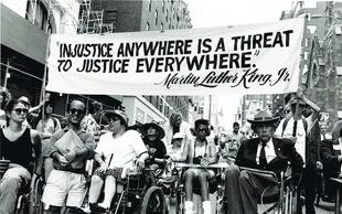 Photo of people with disabilities marching with banner that quotes Martin Luther King, Jr., "Injustice anywhere is a threat to jusitce everywhere."