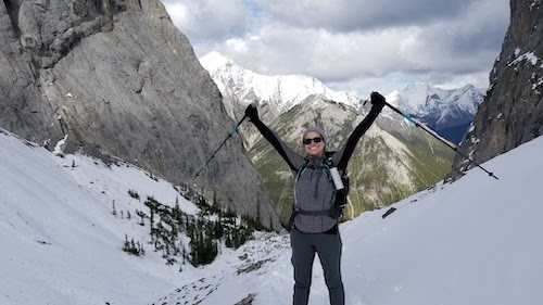 Violet stands on a snowy mountain slope smiling and holding up her ski poles