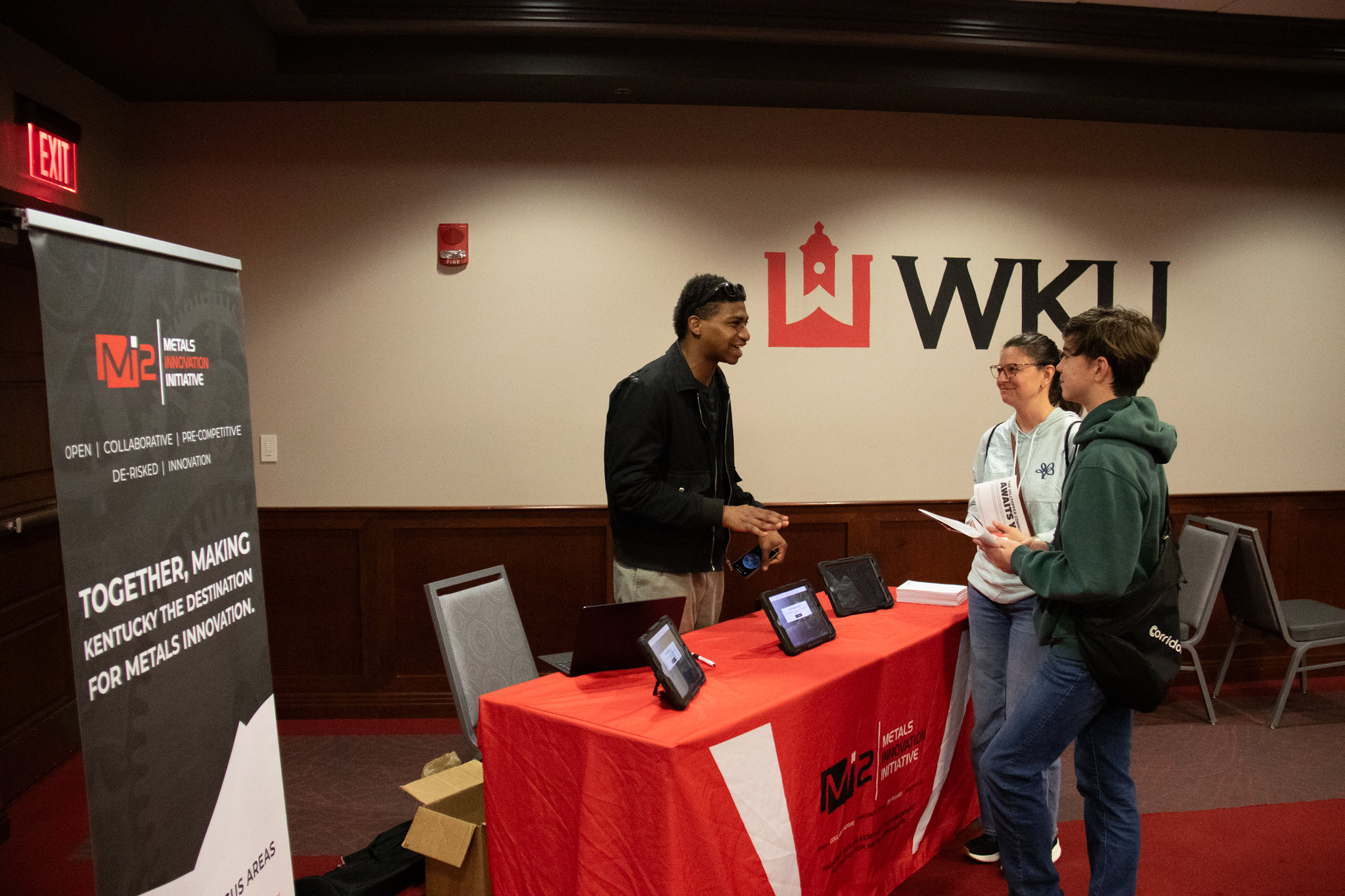 A man from the Metals Innovative Initiative at a booth talking with a mother and son. 