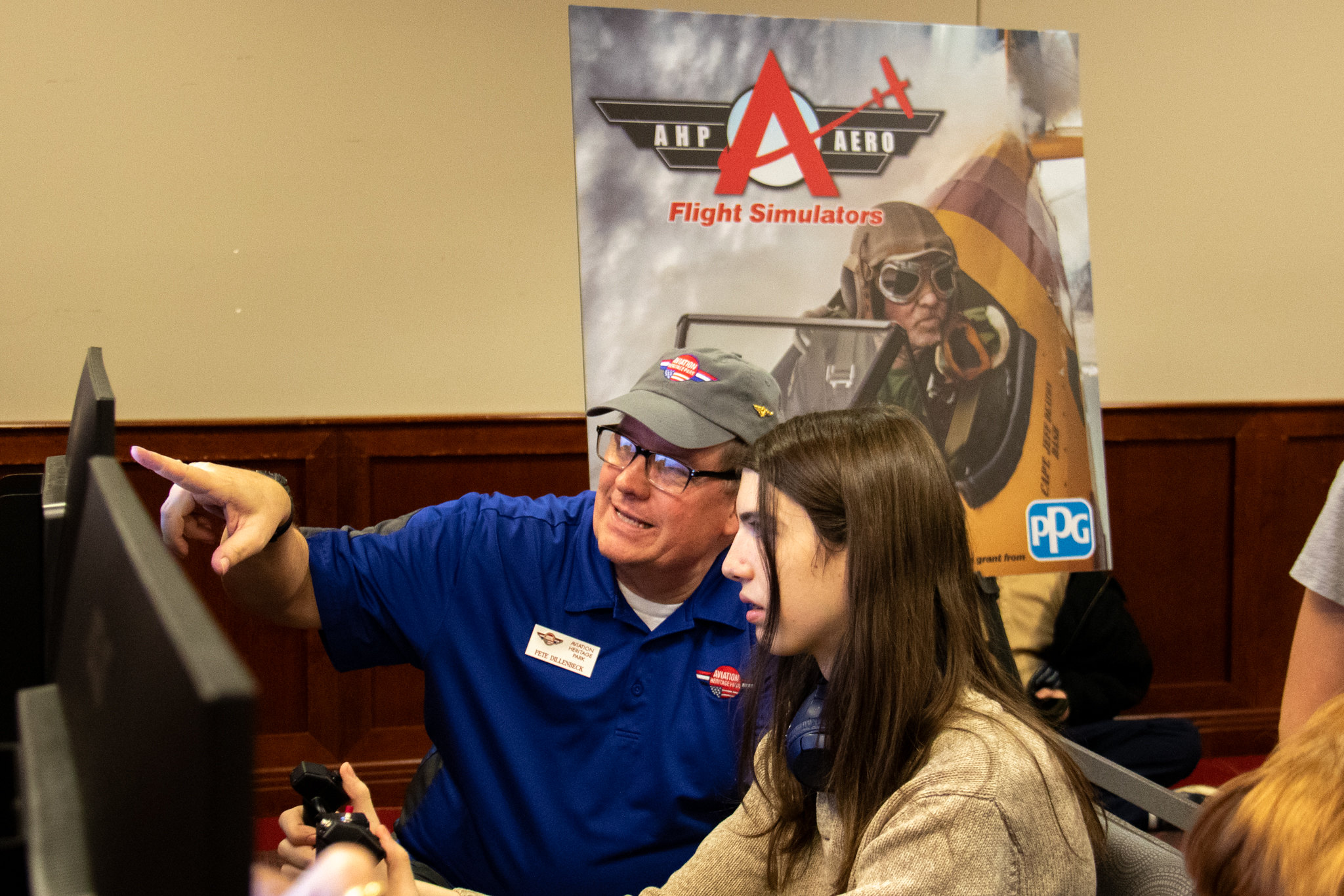 Older man pointing at a screen with an airflight simulation on it as it's controlled by a young student. 