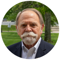 image of man with a full mustache and a dark blazer over a plaid shirt