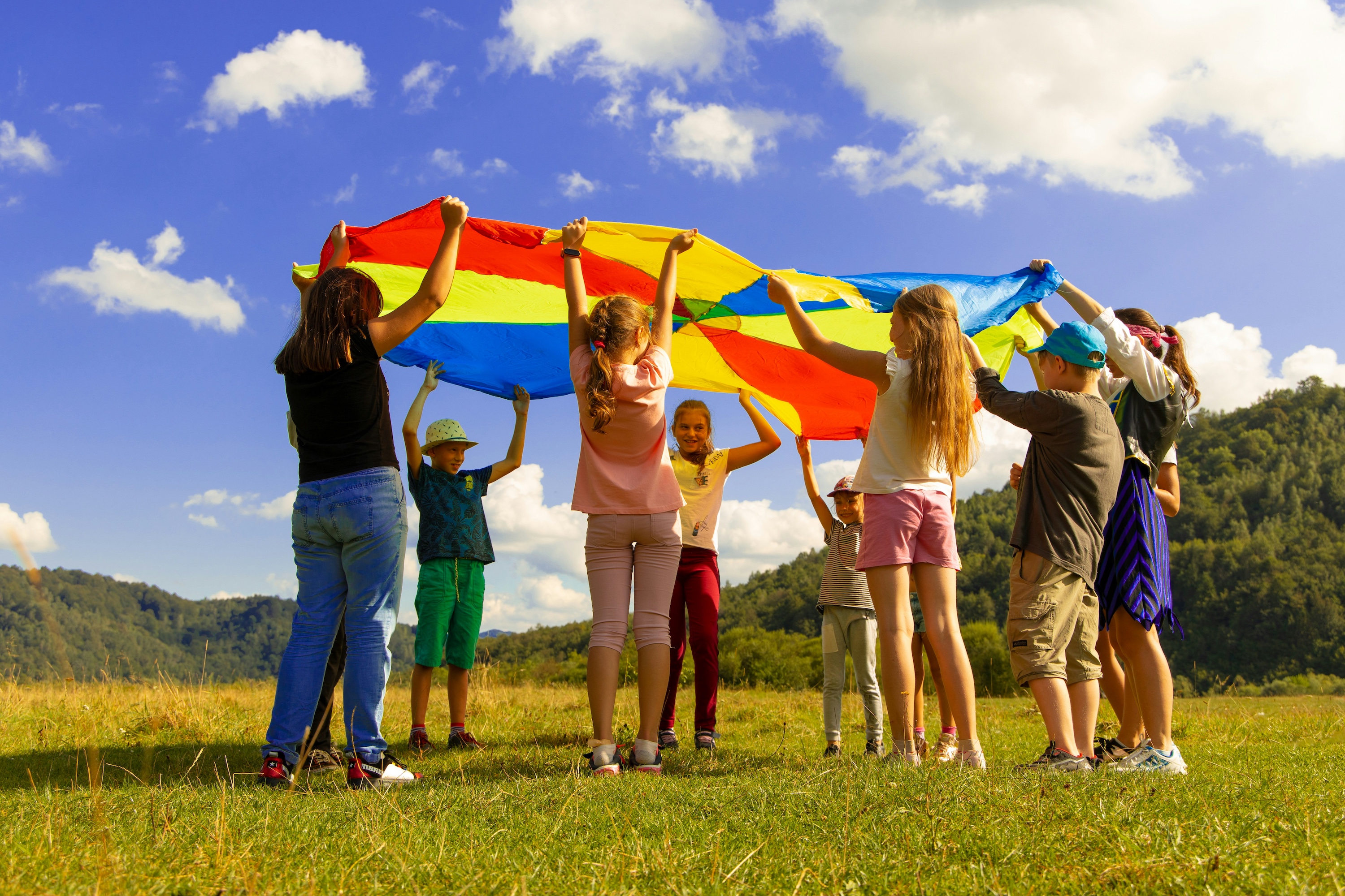 group of children playing outside on grass with a multicolored tarp in the air