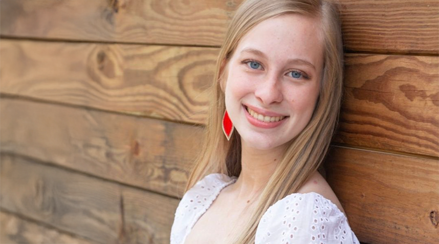 Smiling woman with long blonde hair standing infront of wood plank wall