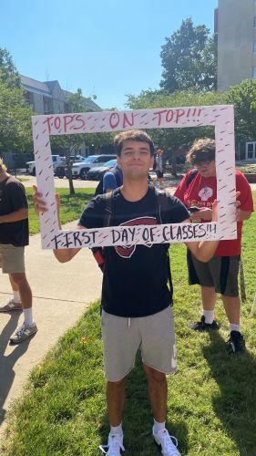 young caucasian man holding a cardboard cutout of a picture frame with himself as the center of the picture