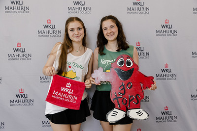 two young women holding WKU symbols smiling in front of a back drop