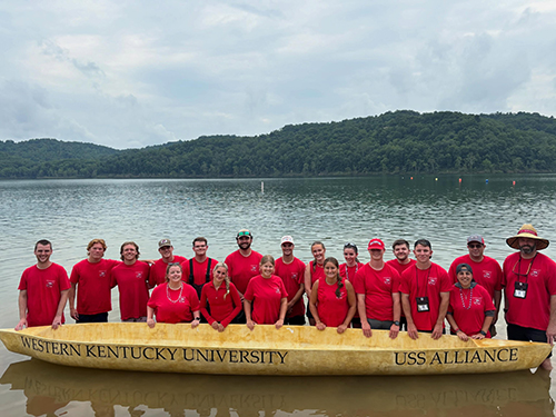 Concrete canoe team stands with their canoe in the lake