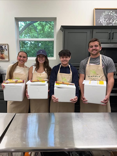 Students pose in aprons with boxes of food
