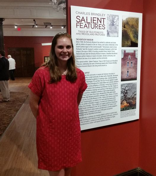 Smiling woman next to a poster about an exhibit