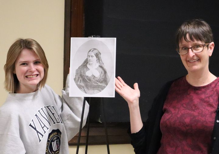 Two women stand on either side of a print of Susan B. Anthony.