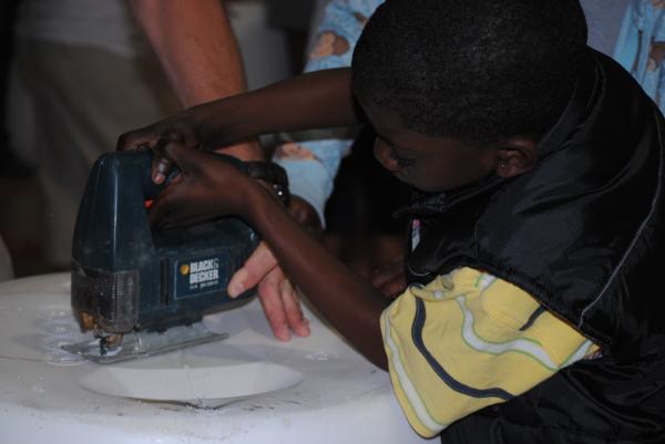 Child uses both hands to guide the jig saw around the mark.