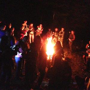 View Participants standing around a bonfire Larger