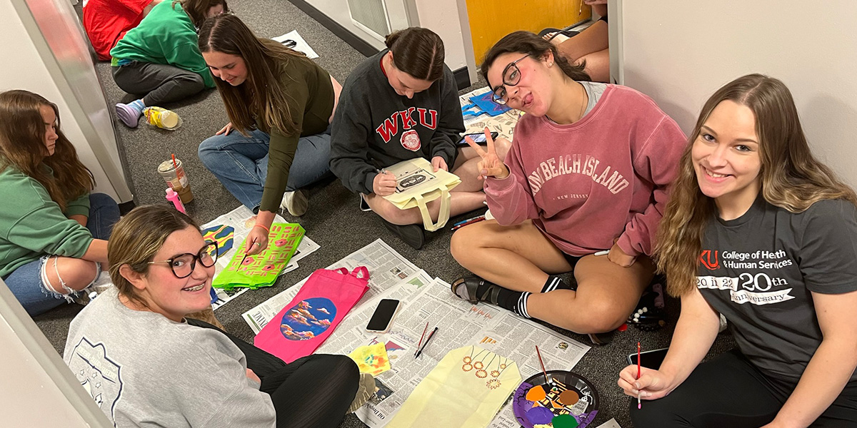 Students painting totes in the hallway of a residence hall