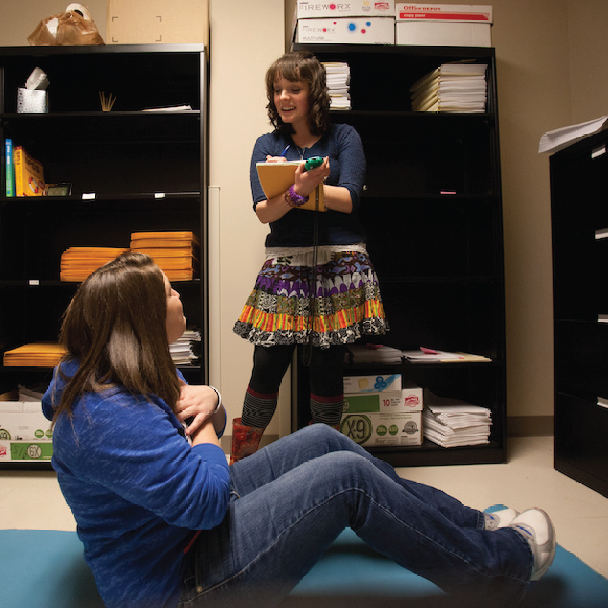 WKU student stands and talks to another student who is on the floor doing sit ups in a Psychological Sciences lab.