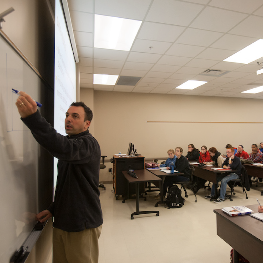 Students watch in background as WKU professor teaches and writes on dry erase board.
