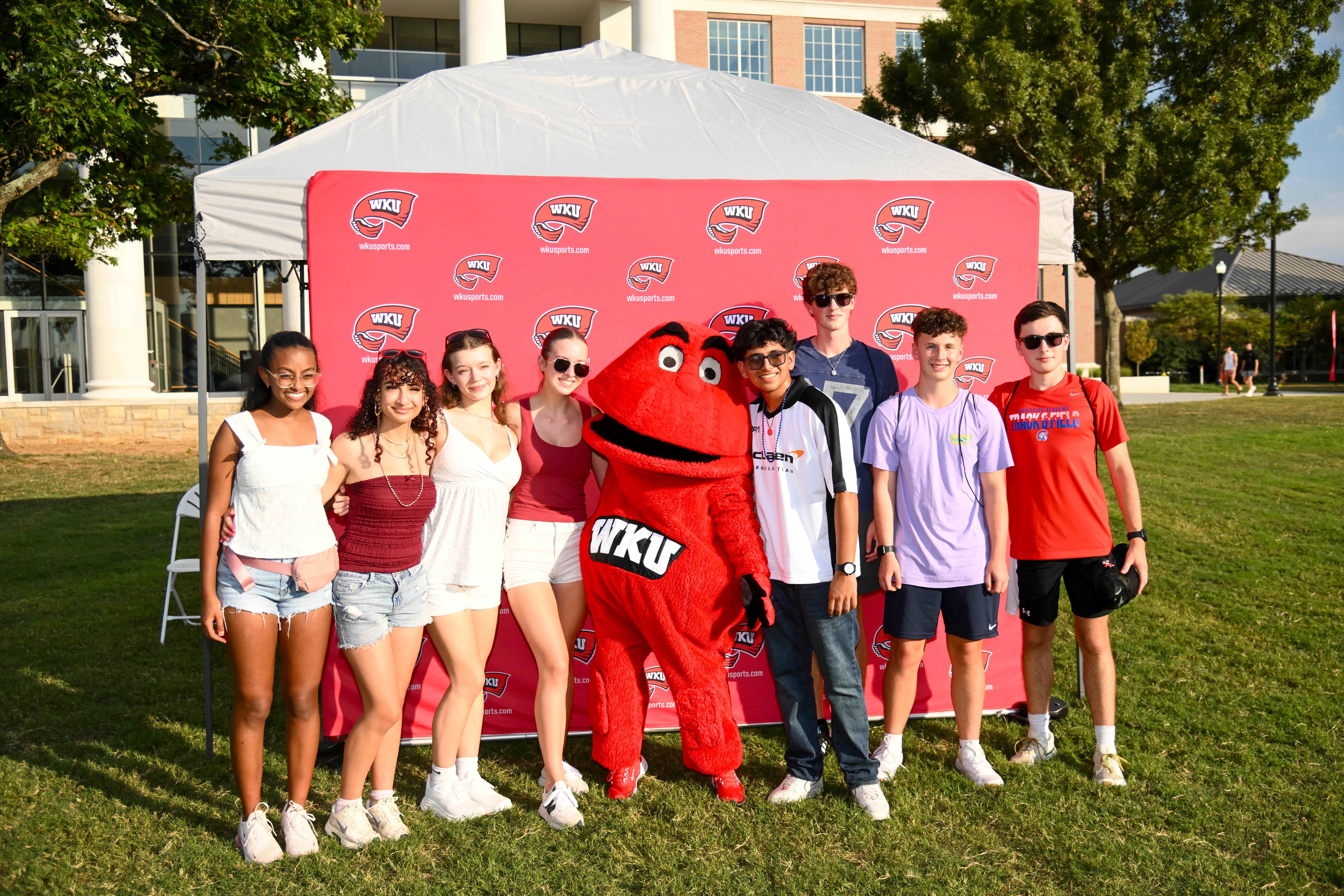 Students posing for a photo with Big Red in front of a WKU backdrop at Topper Fest