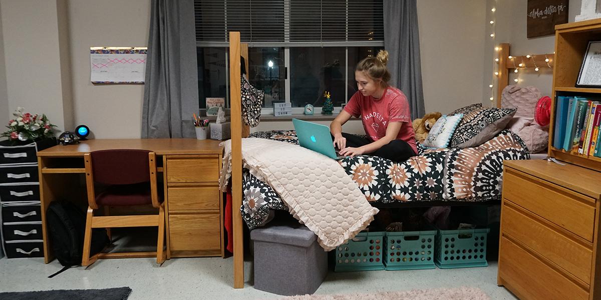 Student sitting on the bed in Southwest Hall
