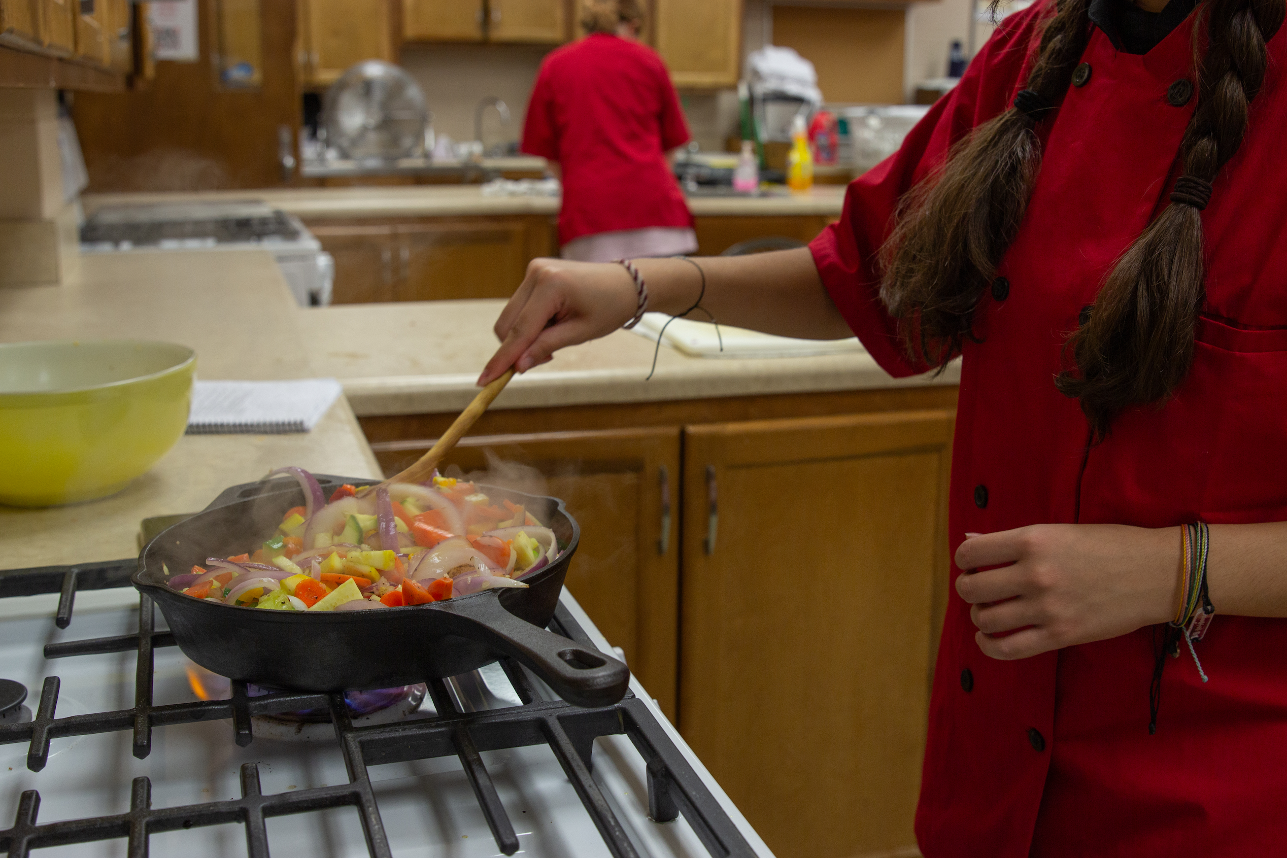A student cooks vegetables in a cast iron skillet.