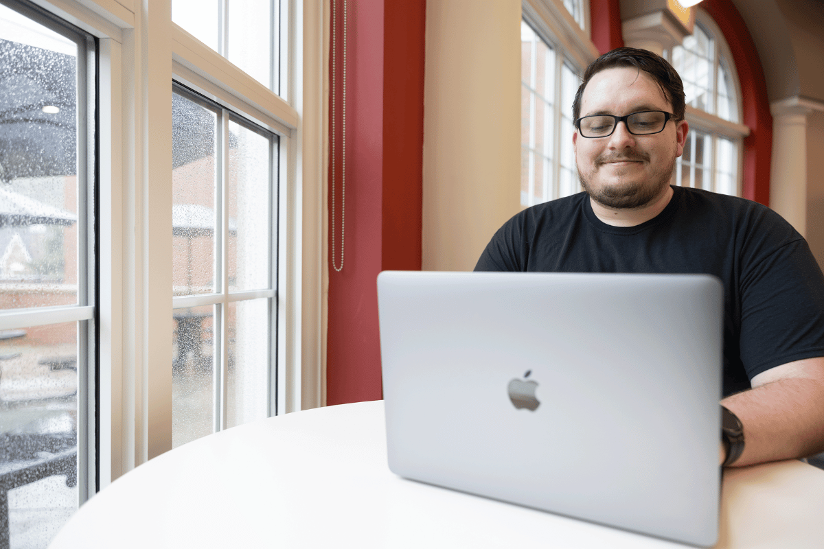 A student studies on a laptop near a window.