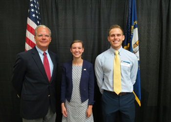 Three people standing by flags.