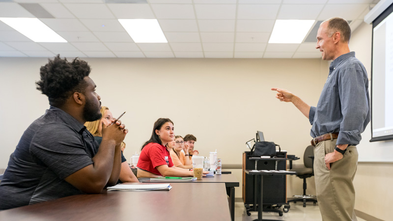 Dr. Steven Wininger gestures while leading a classroom discussion with psychology students seated at desks.