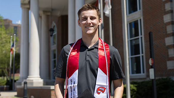 Rowen Wilkinson smiling on campus in front of white pillars, wearing a red and white WKU Student-Athlete graduation stole.