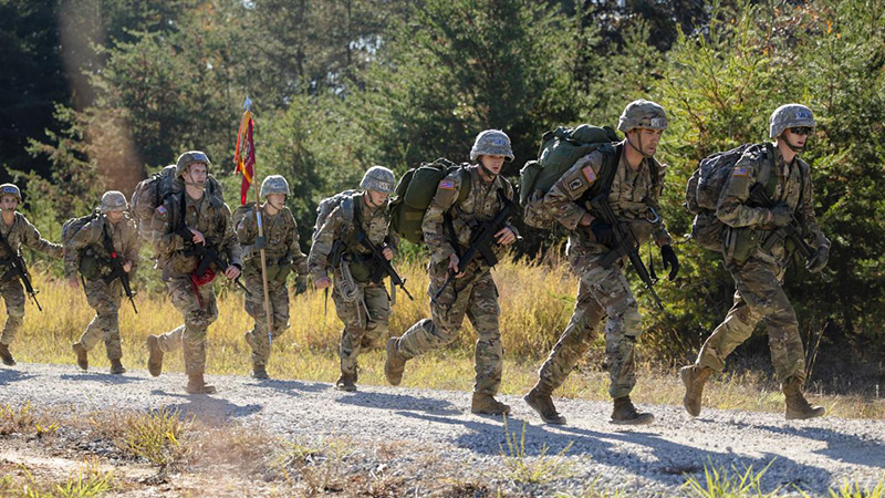 WKU Army ROTC cadets marching in formation across an open field carrying the red Hilltopper Battalion guidon flag.