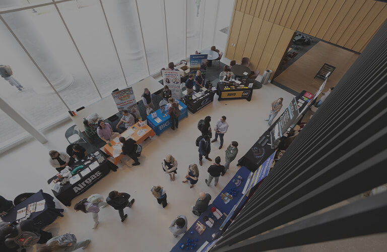 Students and employers gather at business fair booths in a campus atrium, viewed from above