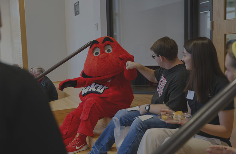 WKU mascot, Big Red, sitting on steps and fist bumping a student