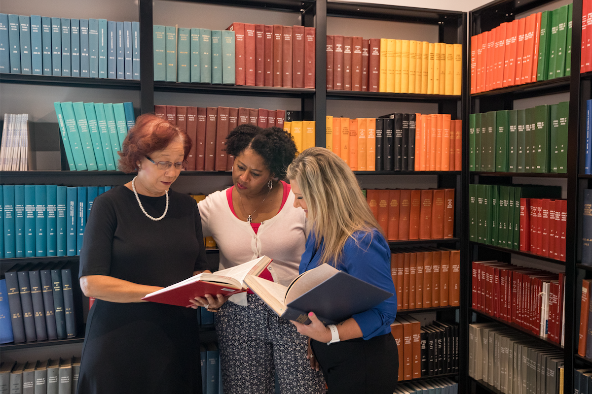 Three adult learners look at a book together.