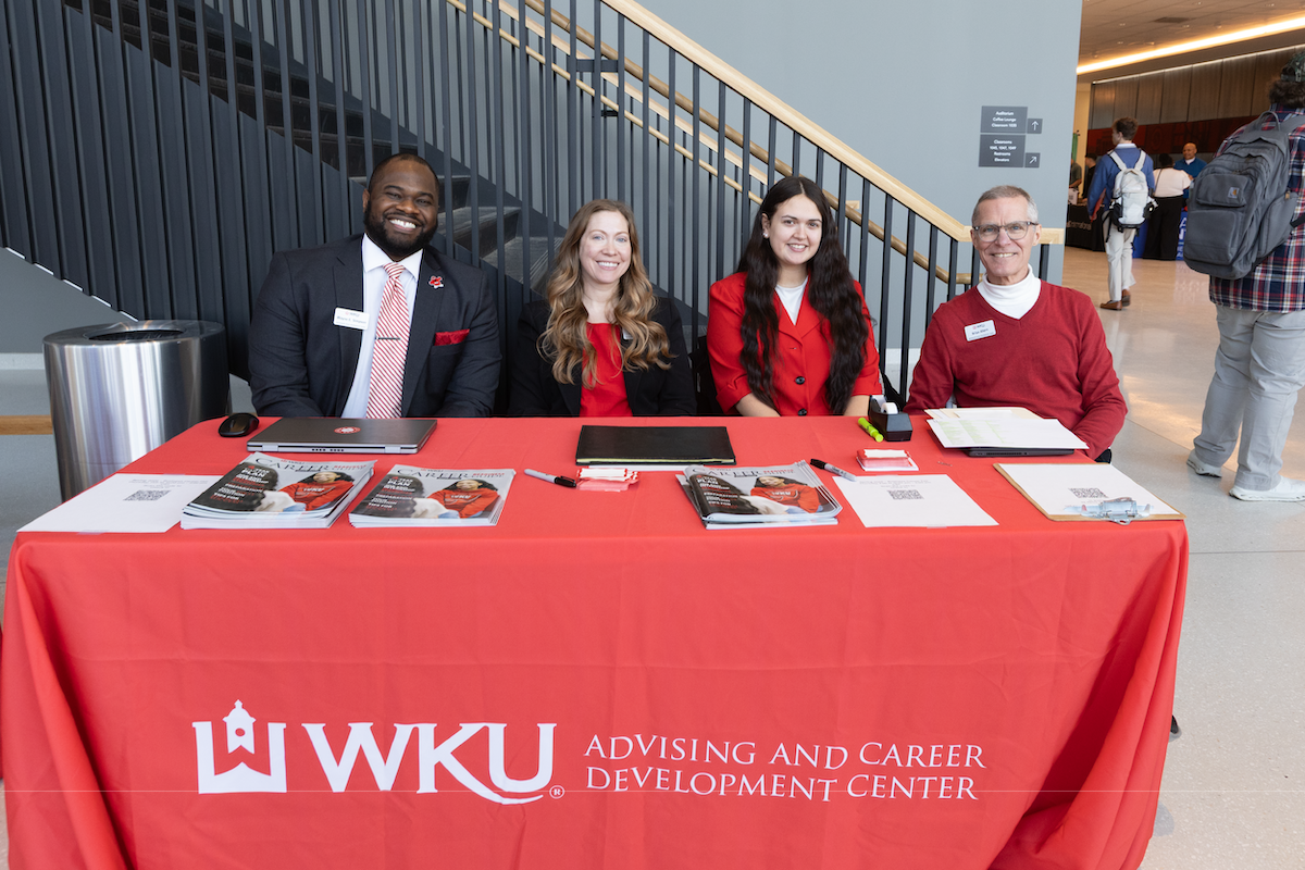 Four representatives of the Academic & Career Development Center sit at a table at a career fair.