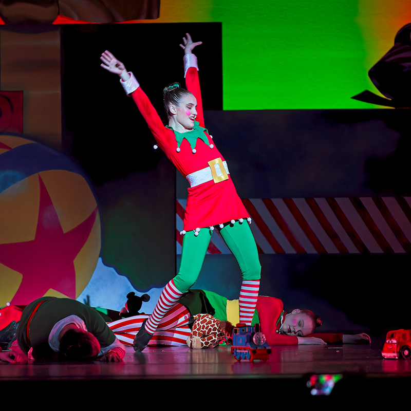 Woman playing an elf on stage with hands in the air..