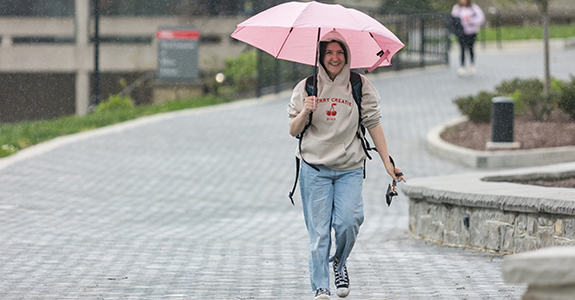 Nicole Johnson, UX Certificate student, walks on campus in the rain holding an umbrella, smiling.